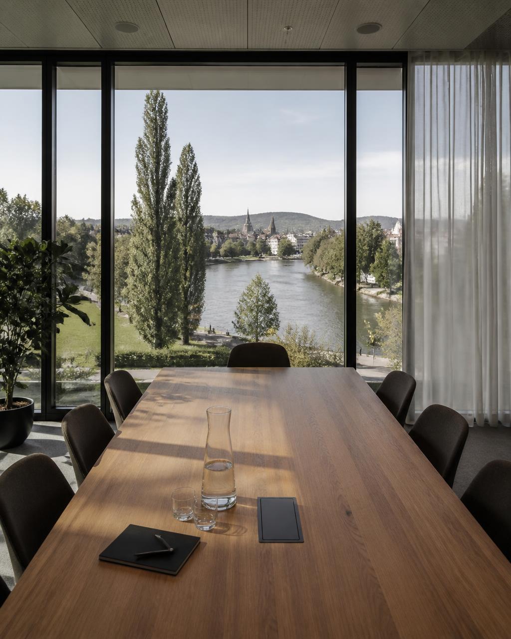 Sitzungszimmer mit Holztisch und Aussicht auf einen begrünten Flusslauf am Stadtrand
